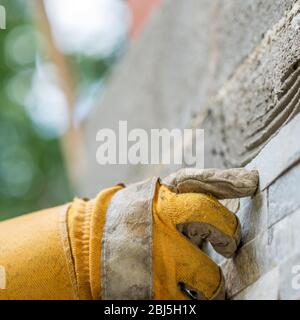 Closeup of a man pressing an ornamental tile into a glue on a wall with gloved hands in a DIY concept. Stock Photo