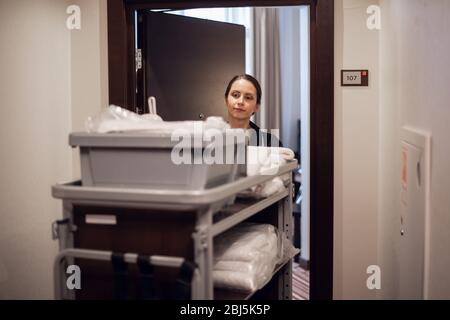 A hotel housekeeper pushing a cleaning supply cart. Stock Photo