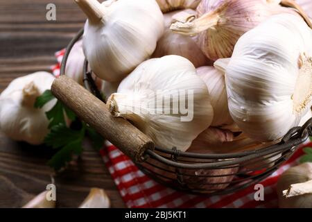 Fresh garlic in the basket decorated with parsley and red checkered cotton napkin on wooden background, close up Stock Photo