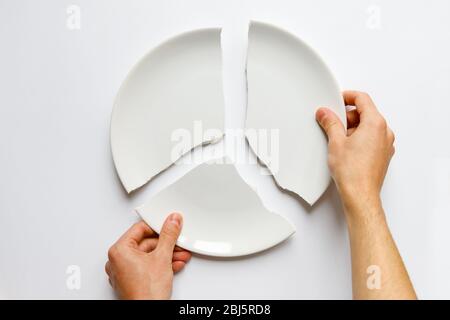 Top view of man hands holding a broken white plate. Metaphor for divorce, relationships, friendships, crack in marriage. Love is gone. Isolated on whi Stock Photo