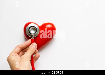 Closeup of man hand holding a red stethoscope on heart - medical diagnostic device for auscultation (listening) of sounds coming from the heart, bronc Stock Photo