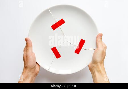 Top view of man hands holding a broken white plate, parts glued with red tape. Metaphor for divorce, relationships, friendships, crack in marriage. Lo Stock Photo