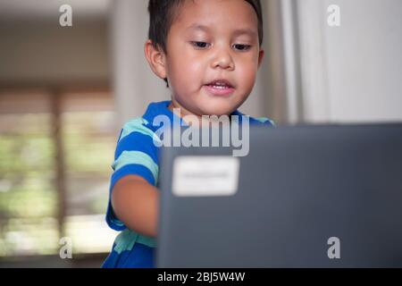 A young boy engaged in distance learning class is using a laptop to continue education. Stock Photo