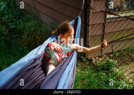 A small girl in a bright colored tutu plays in a hammock in sunshine Stock Photo