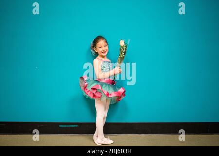 A little girl stands in a dance costume holding a bunch of flowers Stock Photo