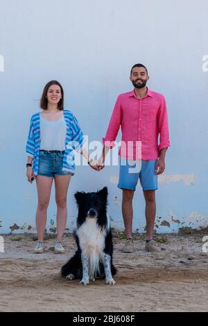 Happy couple standing with dog against wall while holding hands Stock Photo