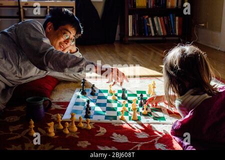 A smiling dad and his young girl play chess in a patch of bright light Stock Photo