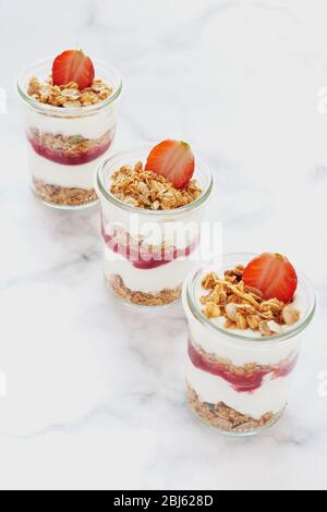 Small jars of granola with yogurt-strawberry jam and fresh strawberries. Healthy-vegan breakfast concept. Focus on the middle. Stock Photo