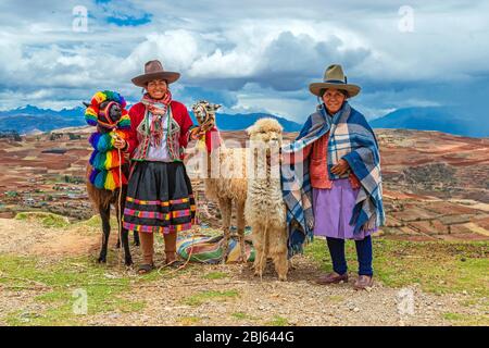 Quechua Indigenous Women in traditional clothing with two llama and one alpaca, Sacred Valley, Cusco, Peru. Stock Photo