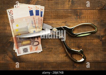Scissors cuts euro banknote on wooden background Stock Photo