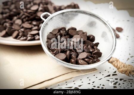 Chocolate morsels on plate, on wooden board Stock Photo