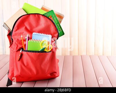 Red backpack full of stationery on wooden table Stock Photo