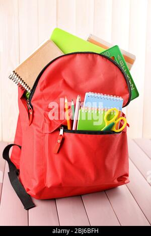 Red backpack full of stationery on wooden table Stock Photo