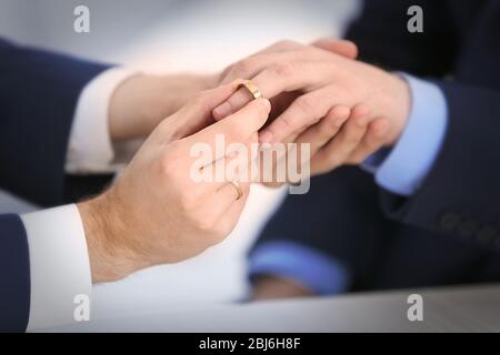 One groom placing the ring on another man's finger Stock Photo