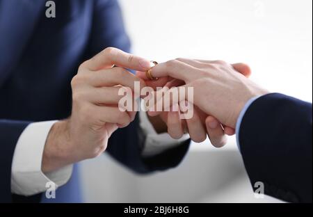 One groom placing the ring on another man's finger Stock Photo