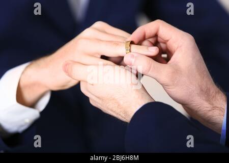 One groom placing the ring on another man's finger Stock Photo