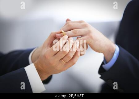 One groom placing the ring on another man's finger Stock Photo