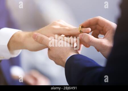 One groom placing the ring on another man's finger Stock Photo