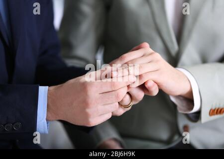 One groom placing the ring on another man's finger Stock Photo