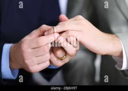 One groom placing the ring on another man's finger Stock Photo