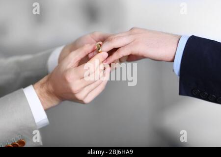 One groom placing the ring on another man's finger Stock Photo