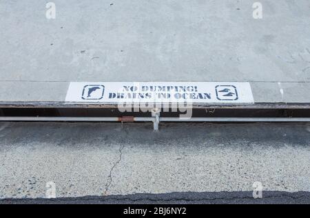 No dumping drains to ocean sign on the sidewalk over a street drain. Southern California USA Stock Photo