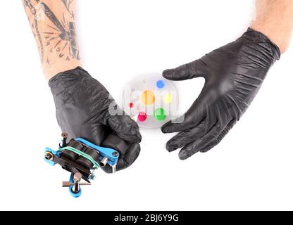 Tattooist hands in black gloves with tattoo machine and colourful inks isolated on white background, close up Stock Photo