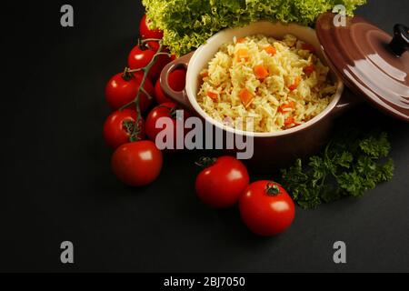 Stewed rice with a carrot and tomatoes in a cooking pot over black background Stock Photo