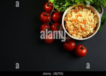 Stewed rice with a carrot and tomatoes in a cooking pot over black background Stock Photo