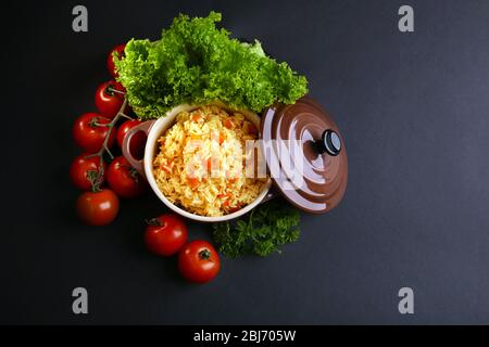 Stewed rice with a carrot and tomatoes in a cooking pot over black background Stock Photo