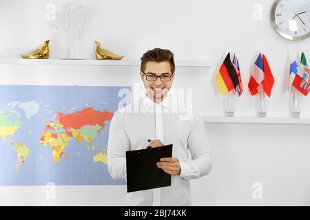 Happy young man with pen and paper holder in the office of travel company Stock Photo
