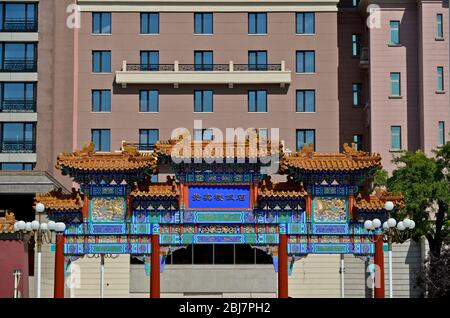 Traditional chinese archway in front of a modern building. Qianmen East Street, Beijing. China Stock Photo