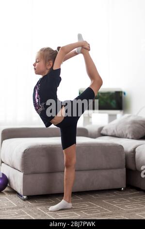 little girl does gymnastics at home doing stretching exercises Stock Photo