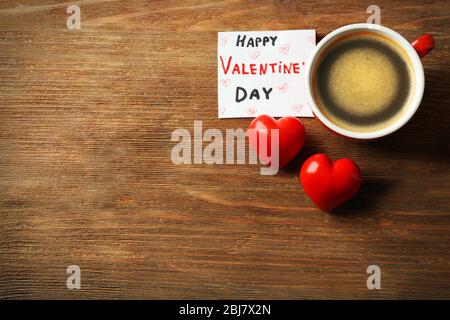 Valentine concept. Cup of coffee with two red hearts and note on wooden table background Stock Photo