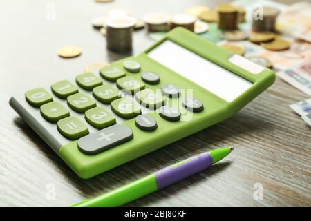 Money concept. Green calculator with banknotes and coins on wooden table Stock Photo