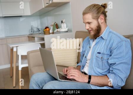Young man elearning from home using laptop sitting on sofa during quarantine. Stock Photo