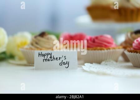 A small Happy Mother's day greeting card before delicious cupcakes and white tulips on a white table, close up Stock Photo