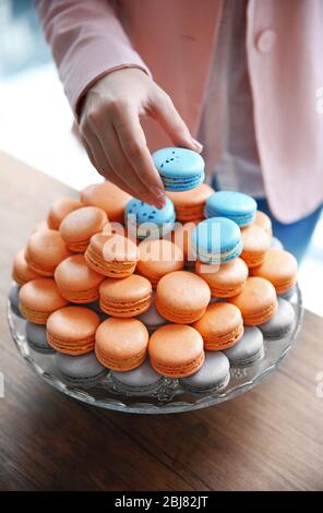 Female hand taking tasty macaroon from dish on the table Stock Photo