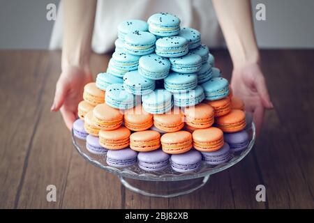 Woman holding varicolored tasty macaroons on glass tray on the table Stock Photo
