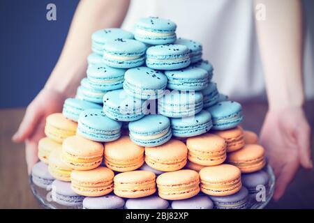 Woman holding varicolored tasty macaroons on glass tray on the table Stock Photo
