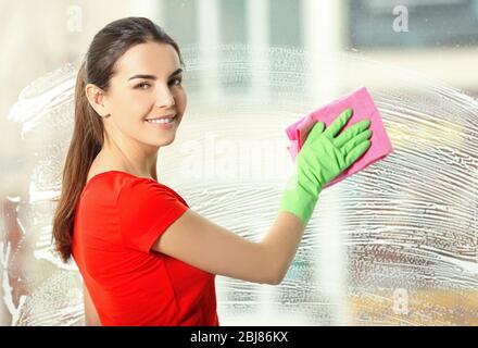 Young woman washing window glass indoors Stock Photo