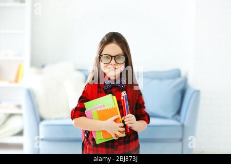 Little girl with red back pack holding notebooks and pencils in living room Stock Photo