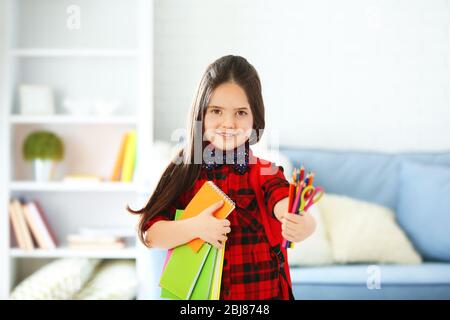 Little girl with red back pack holding notebooks and pencils in living room Stock Photo