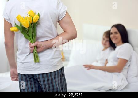 Father holding bouquet of flowers behind for giving to wife in bedroom Stock Photo