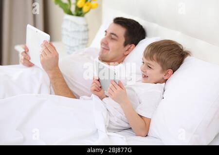 Father and son with tablets lying in bed at home Stock Photo