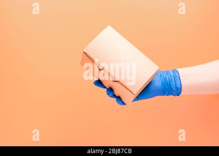 Box with food in hand in a glove on an orange background. Take-away food.  Stock Photo