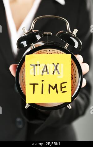 Woman in black suit holding alarm with tax time inscription, close up Stock Photo