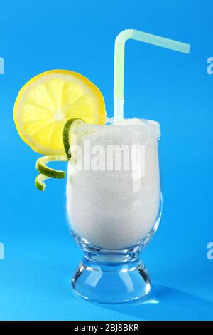 Glass with granulated sugar, cocktail straw and lemon slice on blue background Stock Photo