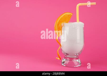 Glass with granulated sugar, cocktail straw and orange slice on pink background Stock Photo