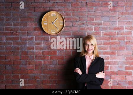 Young attractive woman under the clock, on brick wall background Stock Photo